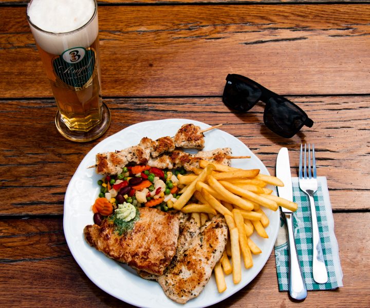 Grilled meat plate with fries, vegetables, beer and sunglasses on a table